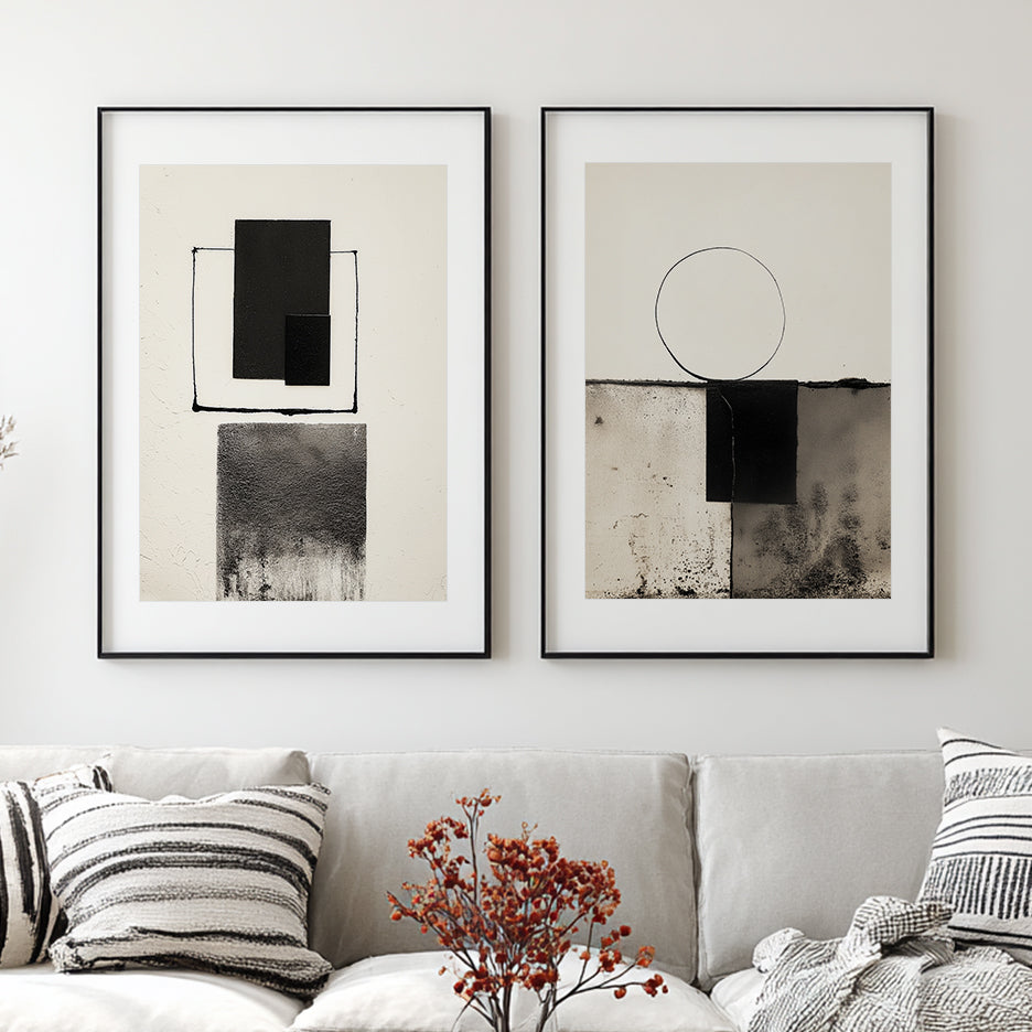 Two framed pieces of Modern Abstract Geometric Wall Art – Minimalist Black & White Textured Print featuring bold black shapes and subtle textured gradients, displayed above a light-colored sofa with patterned cushions.
