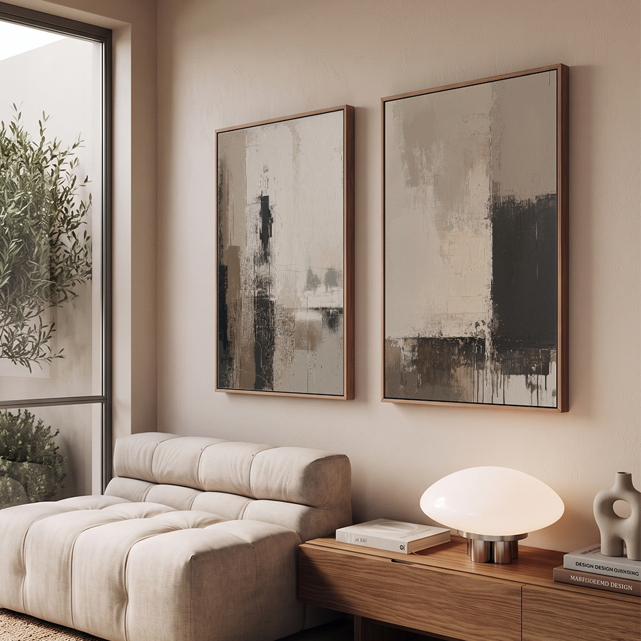 Two framed abstract wall art prints with brown frames hanging on a beige wall above a tufted cream sofa and a wooden side table with a glowing dome lamp.