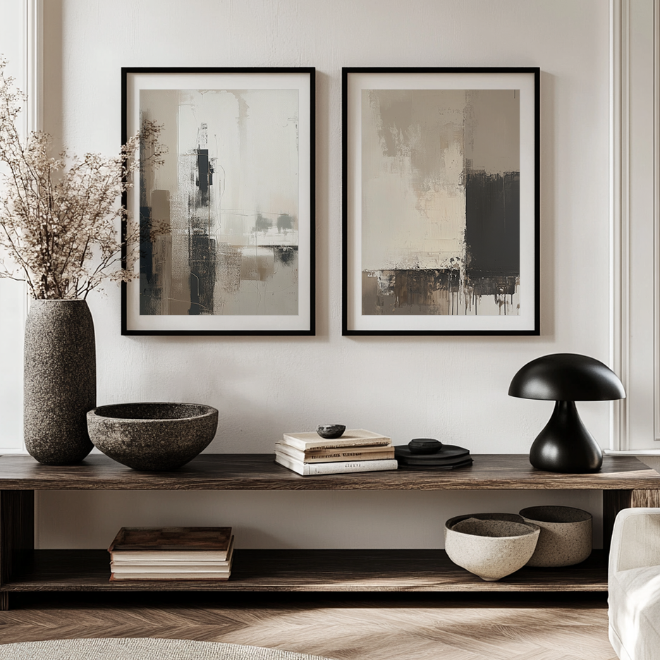 Two framed abstract wall art prints with black frames hang on a light beige wall above a wooden console shelf styled with a vase of dried branches, bowls, books, and a black mushroom-shaped lamp.