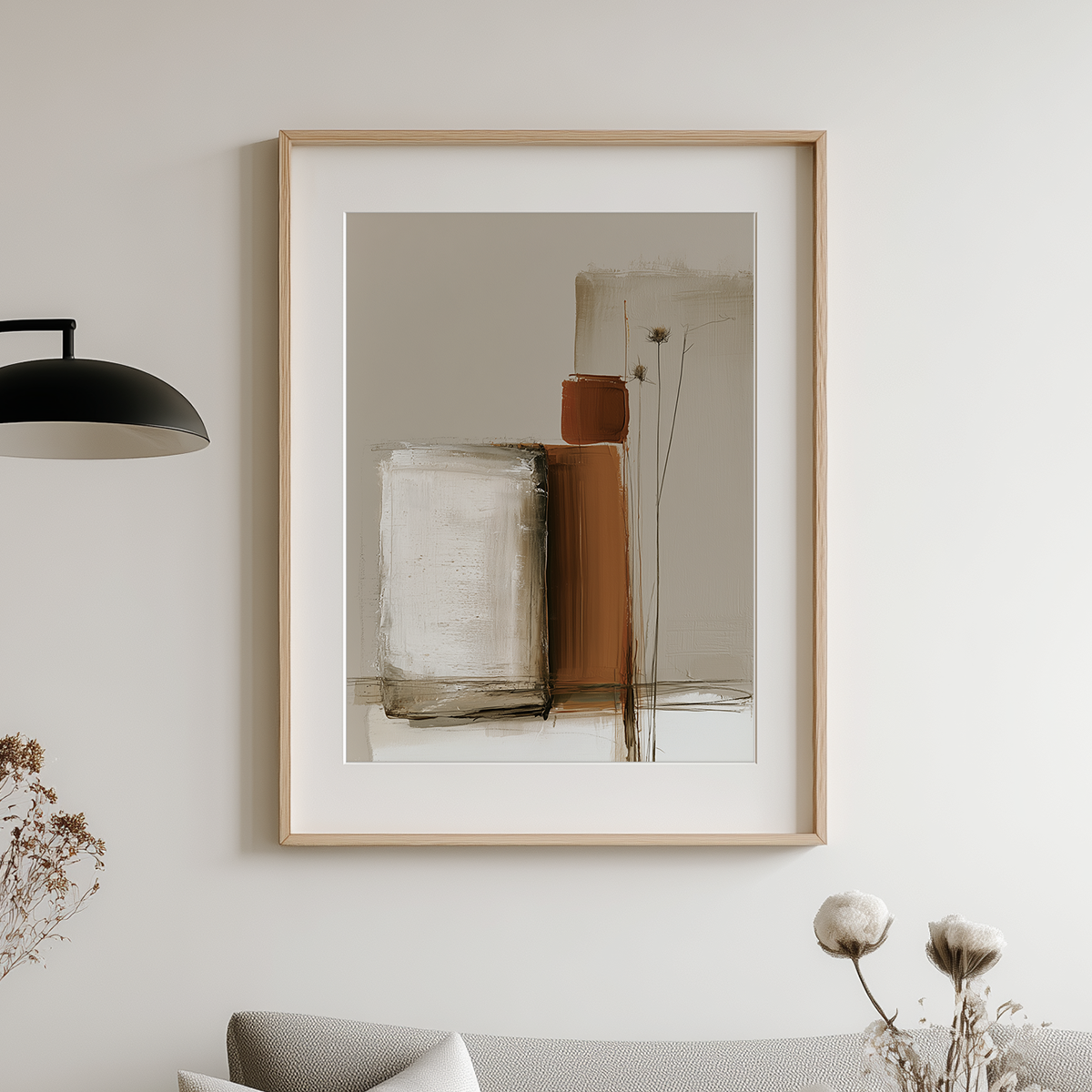 Framed abstract wall art hanging on a light gray wall above a sofa, with a black pendant lamp on the left and dried flowers in the foreground.