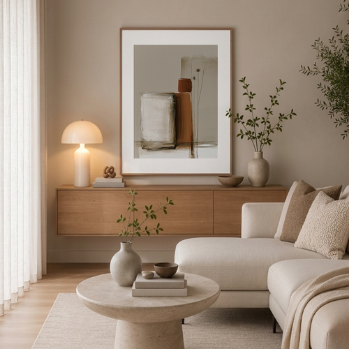 A framed abstract art print with a white mat and light wood frame hangs on a beige wall above a wooden console in a modern, neutral-toned living room with a cream sofa, table lamp, and ceramic vases.