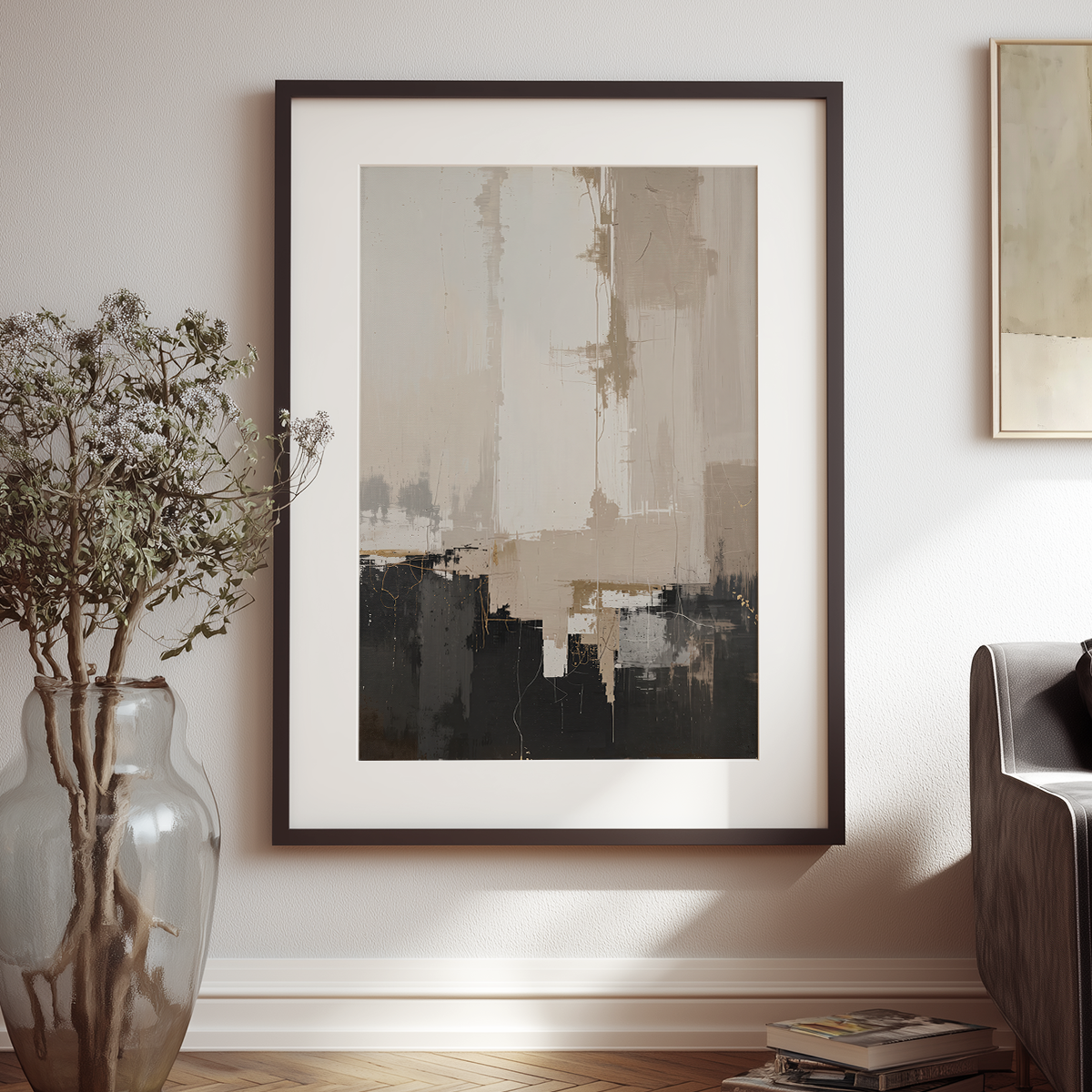 A framed abstract wall art print hangs on a light beige wall in a styled interior. The artwork features layered brushstrokes in beige, taupe, black, and gray, enclosed in a dark frame with a white mat.