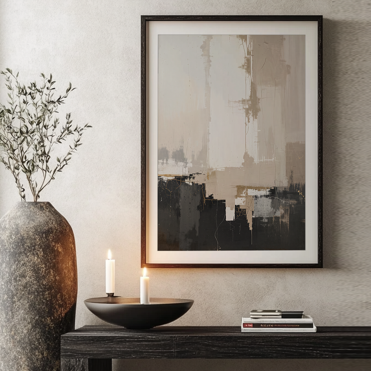 Framed abstract wall art hanging above a dark console table, with a large textured vase, candles, and books in a styled interior setting.