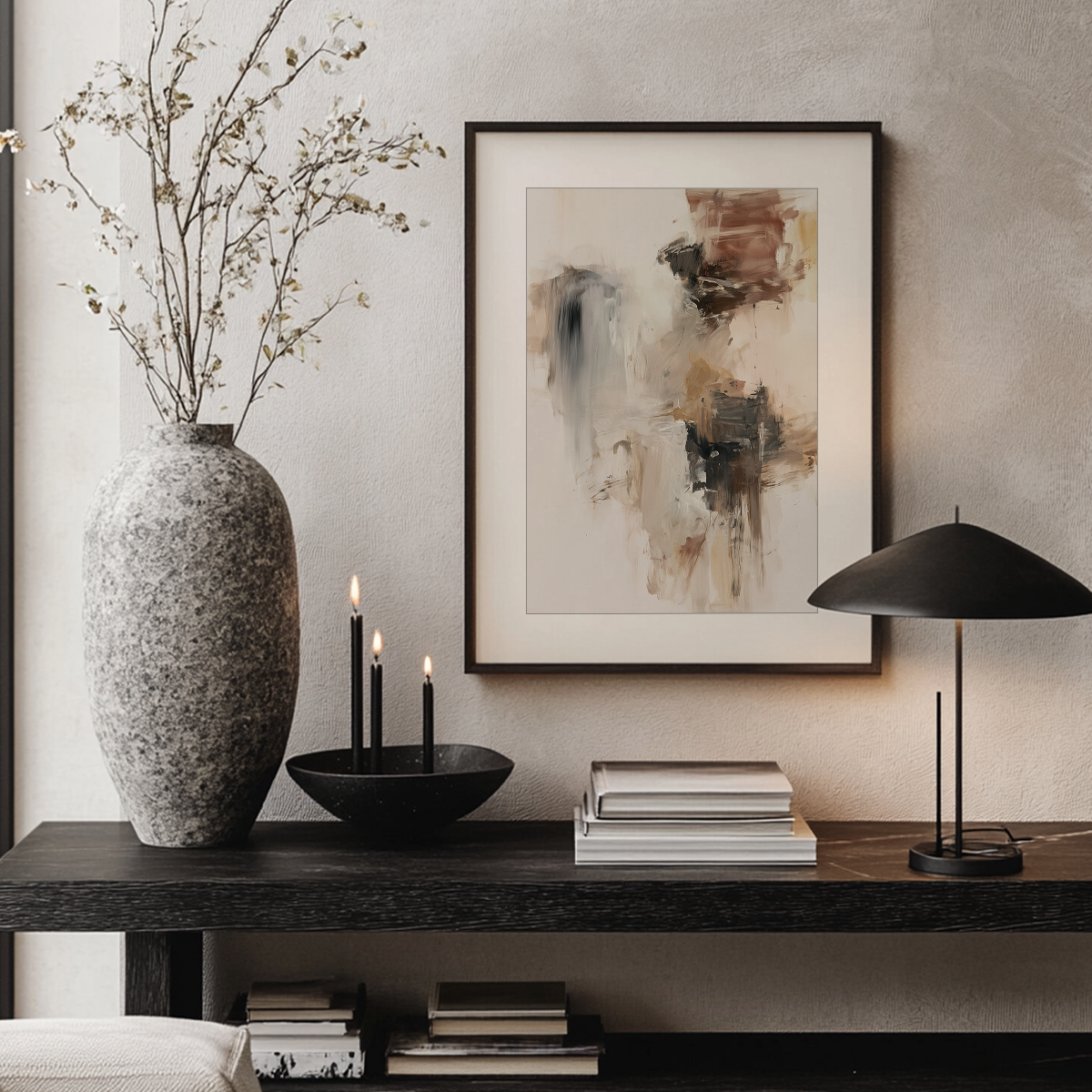 A framed abstract art print hangs on a textured beige wall above a dark wood console table styled with a large speckled gray vase, black candles, a black bowl, books, and a black table lamp.