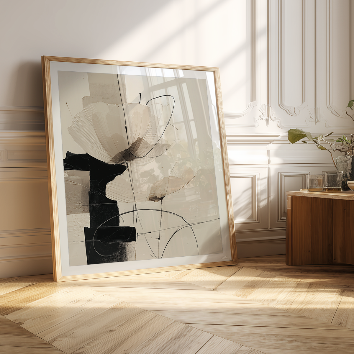 Neutral Abstract Botanical Wall Art Print - Modern Geometric Minimalist Decor featuring soft beige and black floral shapes in a wooden frame leaning against a white decorative wall in natural sunlight.