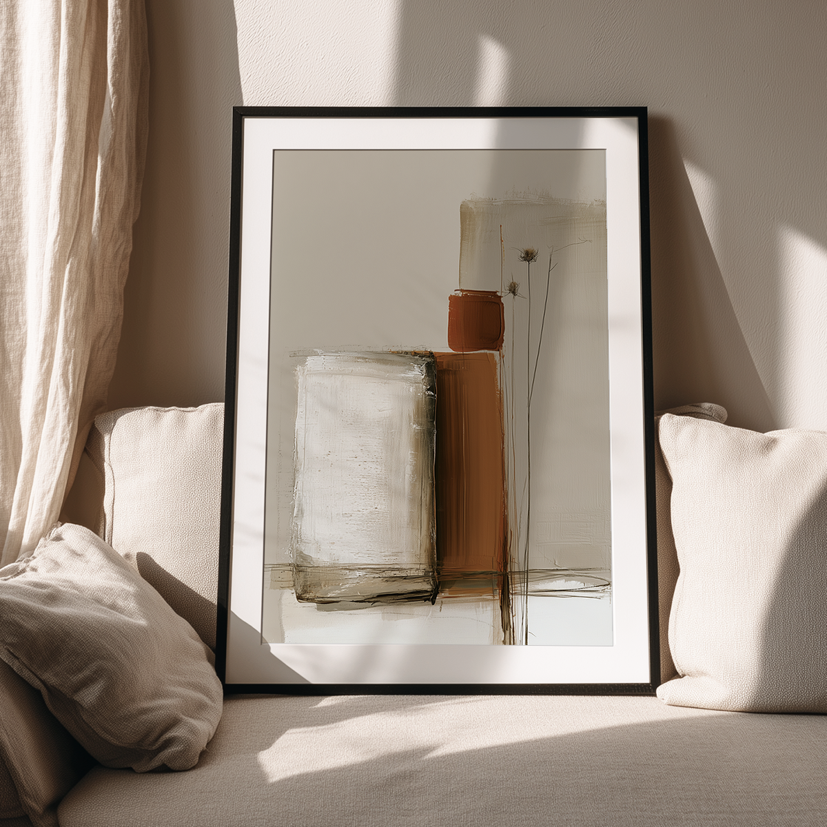 A framed abstract art print with a minimalist design in beige, brown, and white tones, leaning against a wall on a light beige sofa with pillows in a sunlit room.