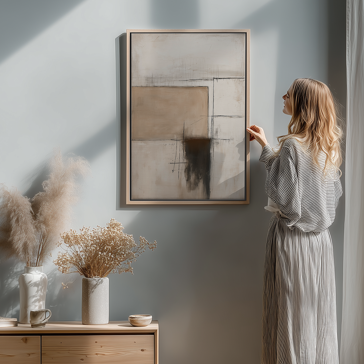 Woman admiring Architectural Abstract Wall Art | Neutral Textured Minimalist Canvas | Wabi-Sabi Modern Decor hanging on a light gray wall in a softly lit modern room with neutral-toned dried flowers.
