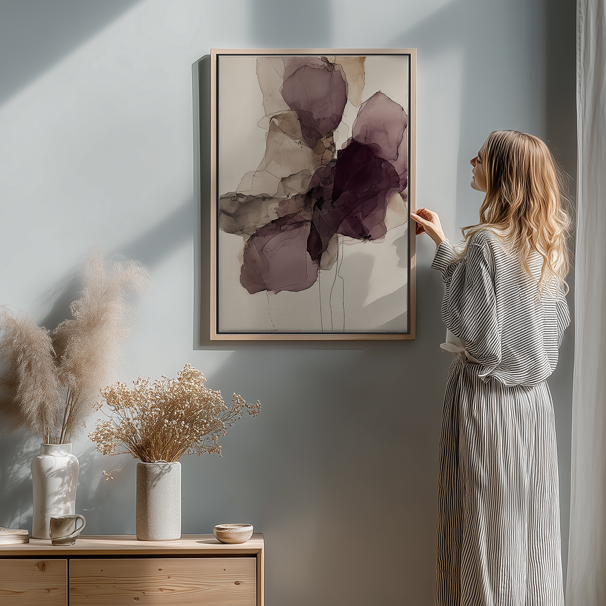 Woman in striped dress adjusting Ink Wash Abstract Floral Wall Canvas Art Print - Burgundy Minimalist Modern Wall Art featuring fluid deep burgundy and taupe floral shapes on muted background in softly lit contemporary room.