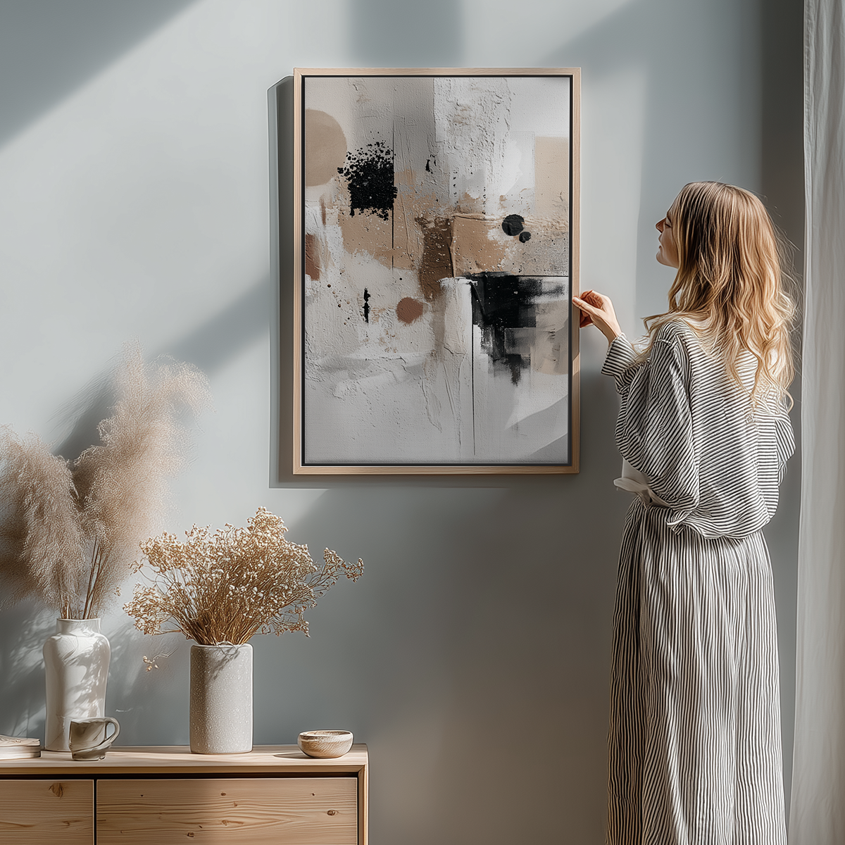 Woman in striped dress admiring Neutral Textured Abstract Wall Art | Japandi Minimalist Canvas in a softly lit modern room with dried floral arrangements and minimalist decor.