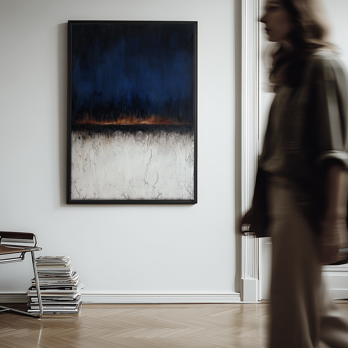 Moody Horizon Abstract Wall Art | Dark Minimalist Landscape Print | Navy & Burnt Orange Decor hanging on a white wall in a modern room with a blurred person walking by and a chair with stacked magazines nearby.