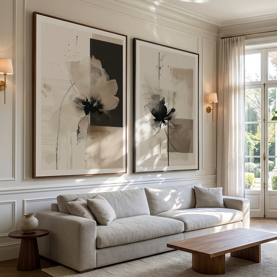 A styled living room featuring two large framed abstract floral wall art prints in black, white, and beige tones, hung above a light beige sofa. The room is decorated with warm wall sconces, a wooden coffee table, and a window with sheer curtains.